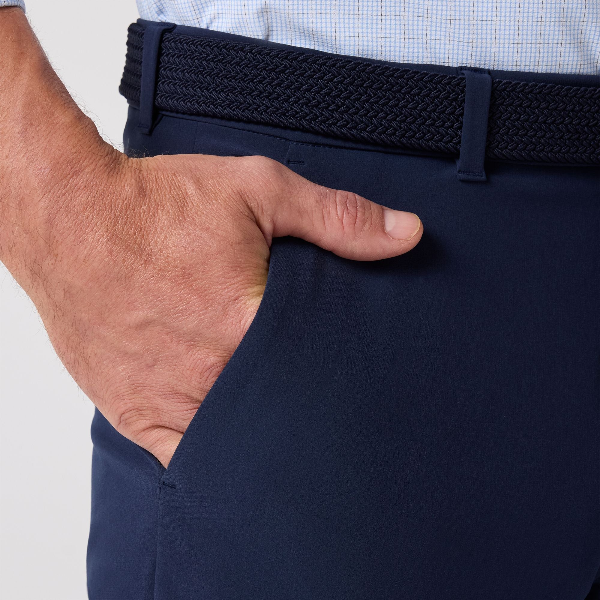 Navy pants with a hand adjusting the waistband on a light gray background