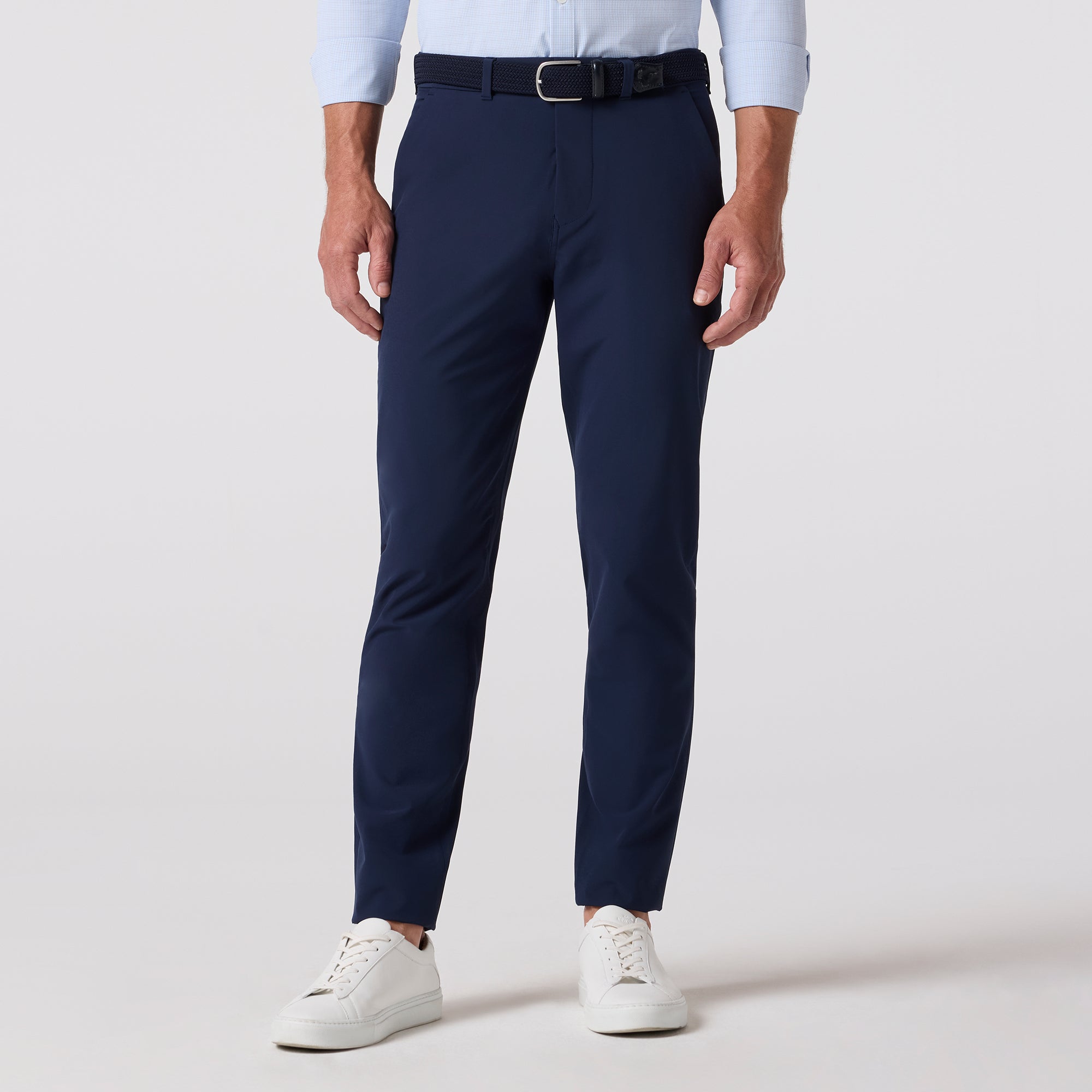 Person wearing navy pants with a white shirt and white sneakers on a light gray background
