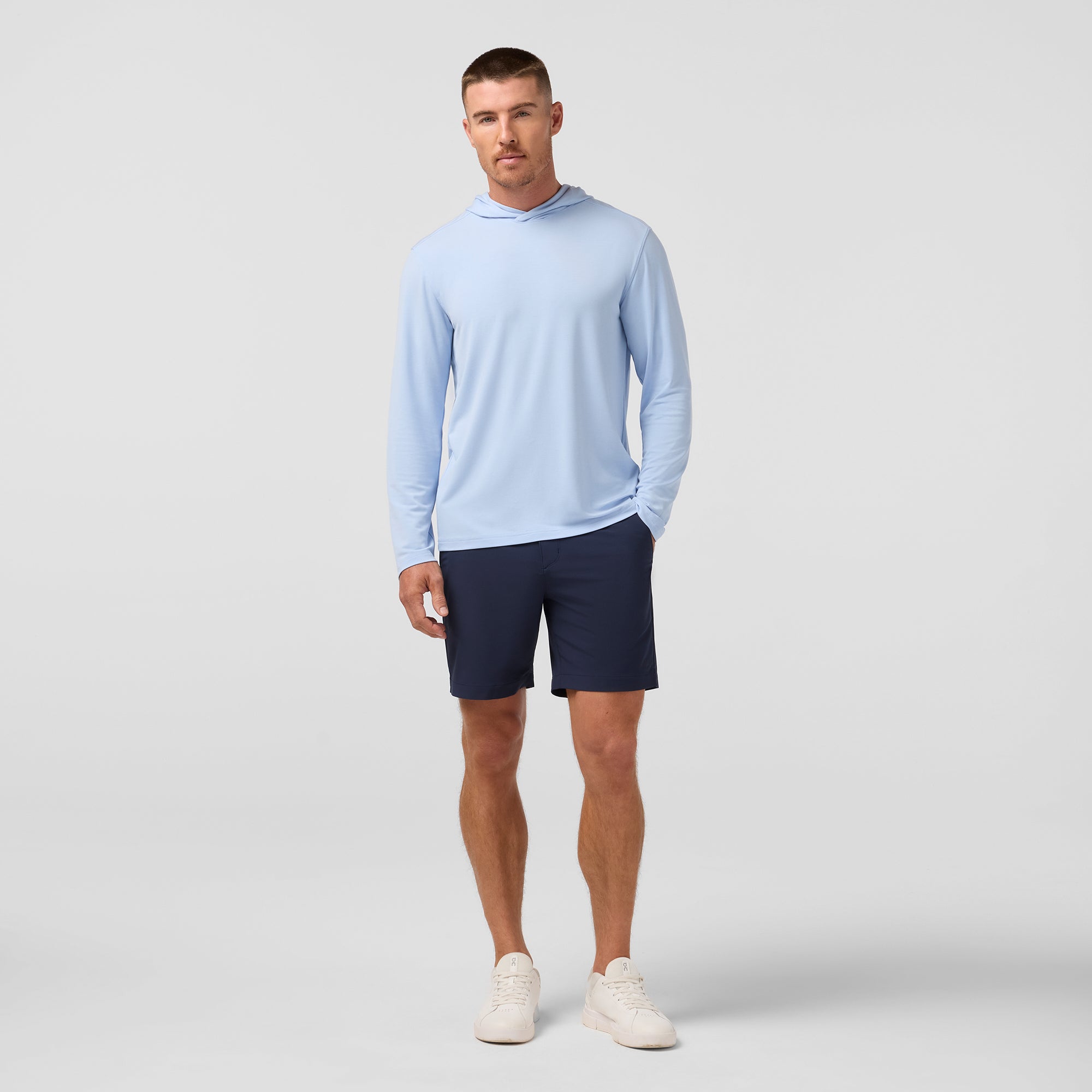 Man wearing a light blue long-sleeve shirt and navy shorts on a gray background