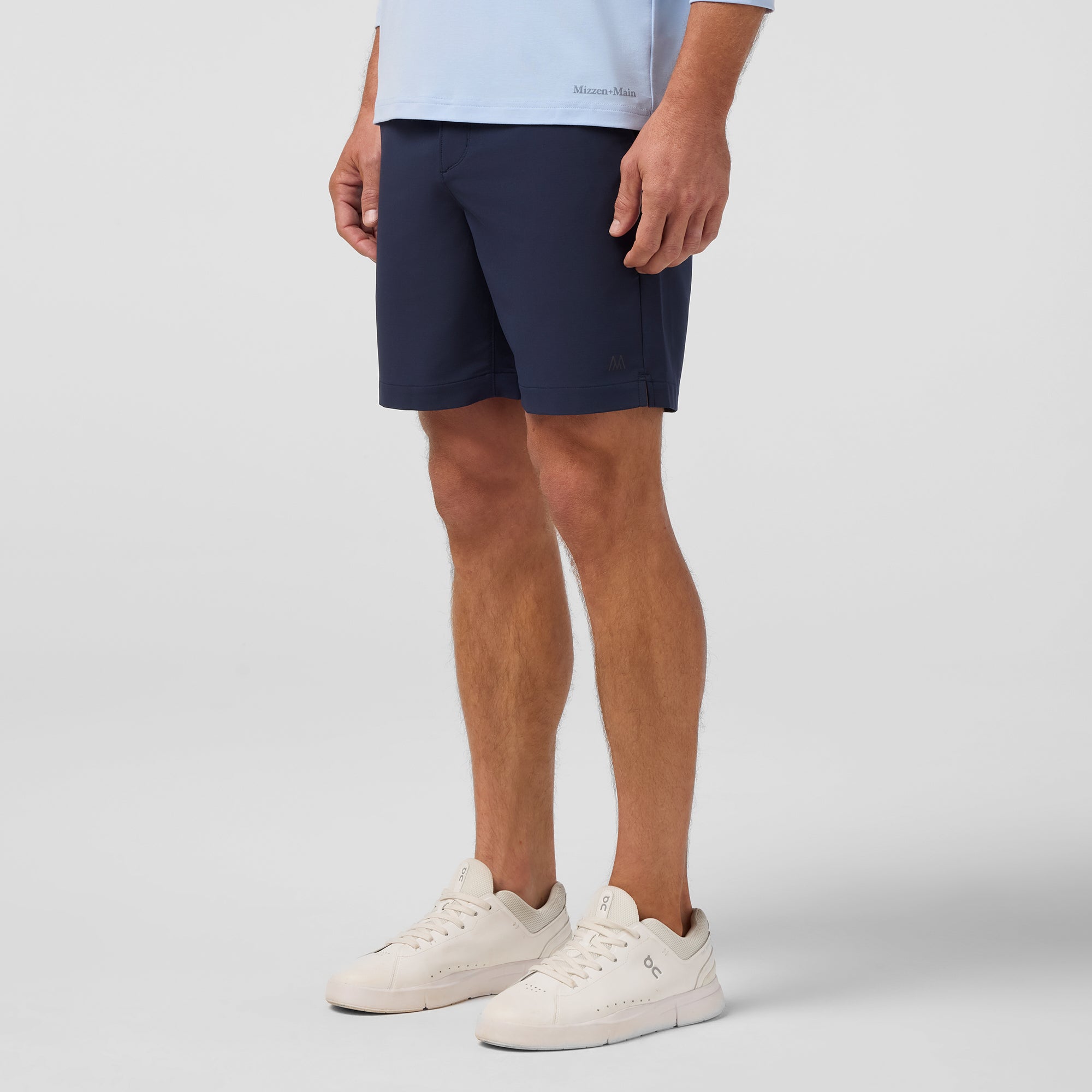 Person wearing navy shorts and white sneakers on a light gray background