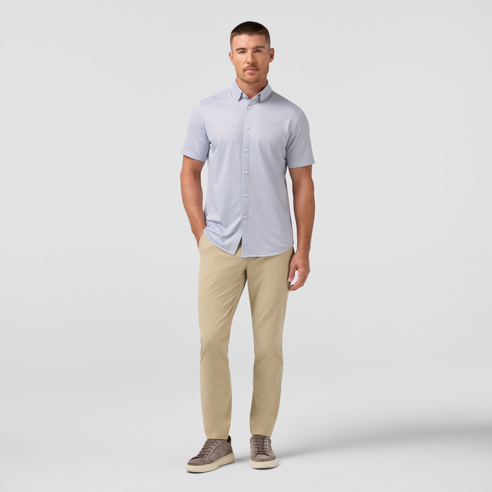 Man wearing a light blue button-up shirt and beige pants on a white background
