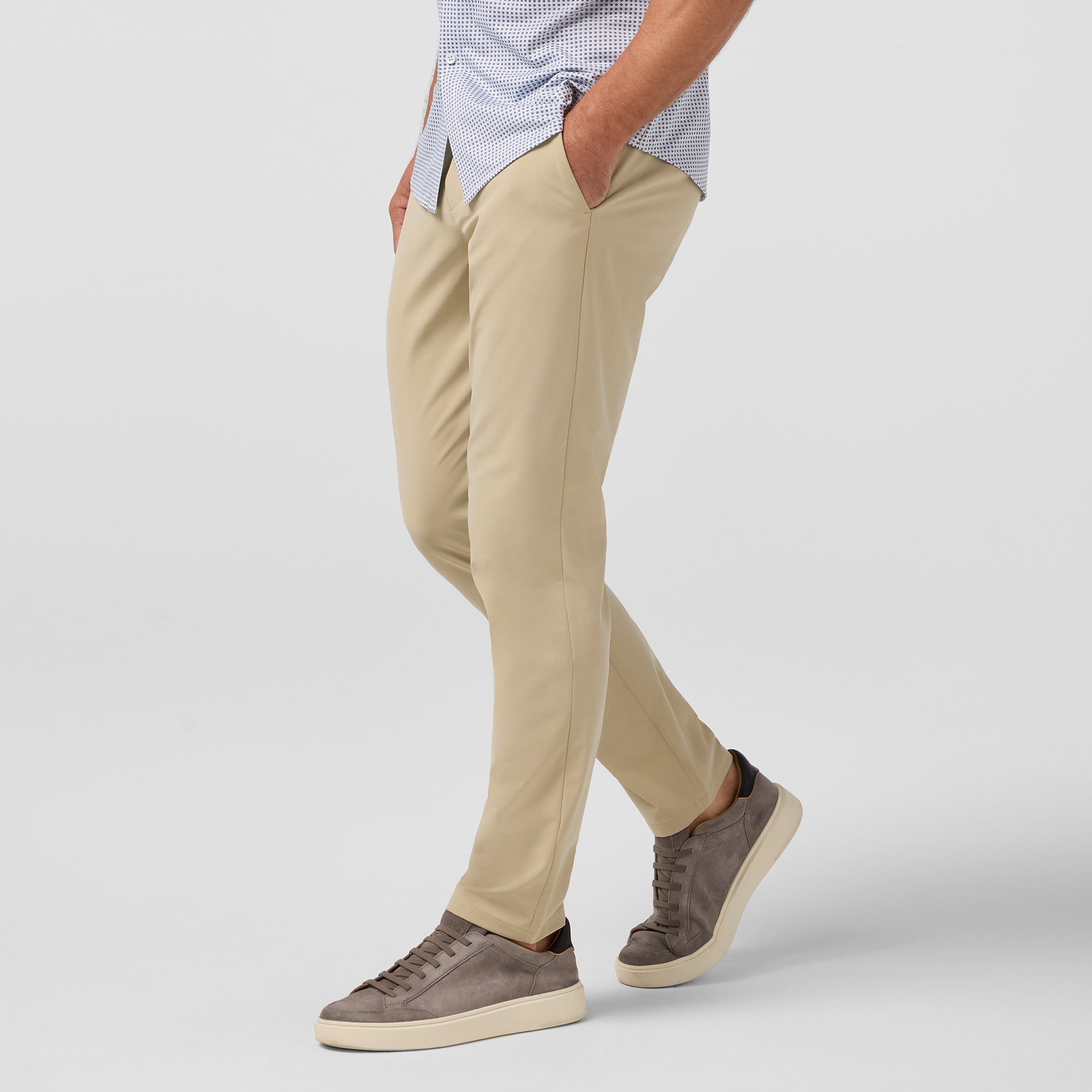 Person wearing beige pants and brown shoes on a plain background