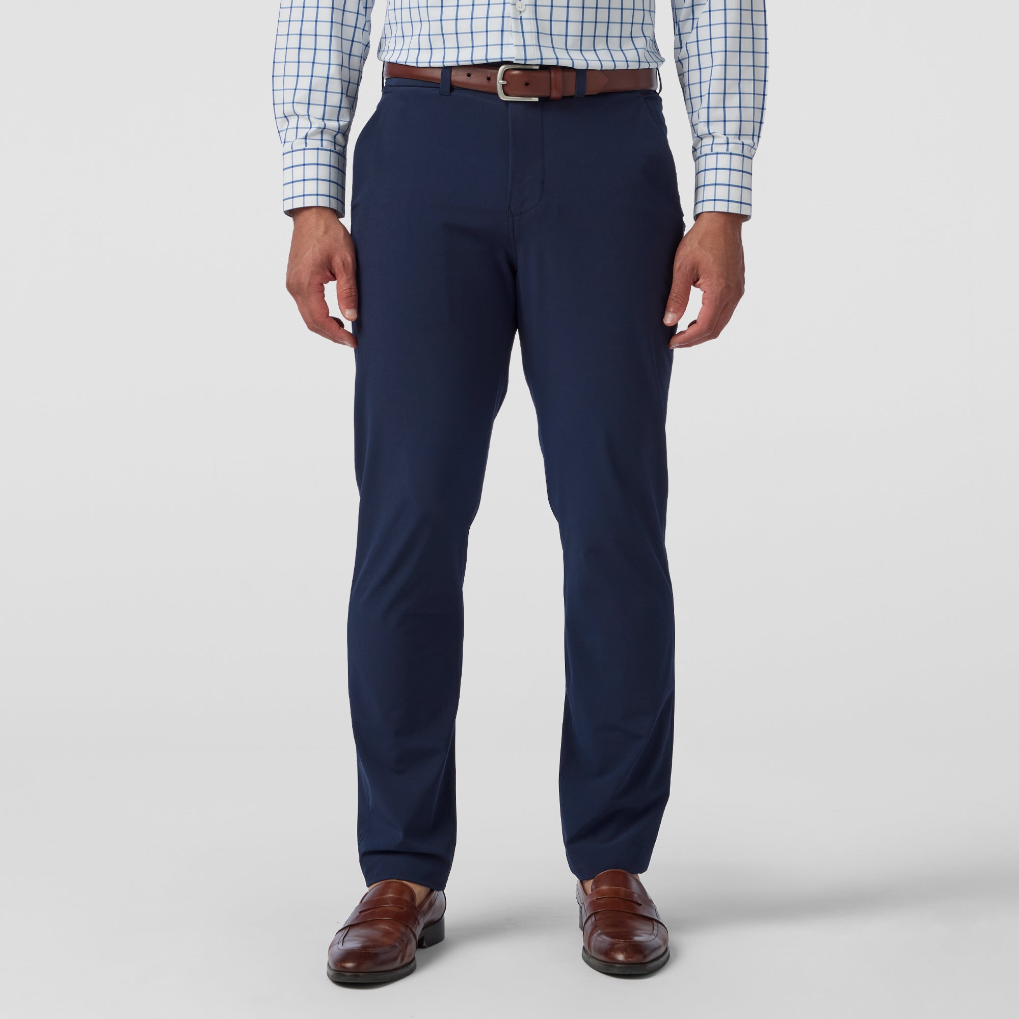Person wearing navy dress pants with a white shirt and brown shoes on a light gray background