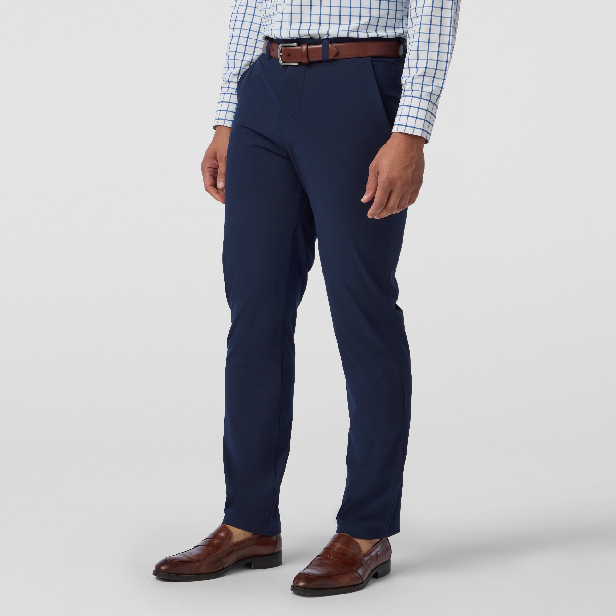Person wearing navy dress pants with a white shirt and brown shoes on a light gray background