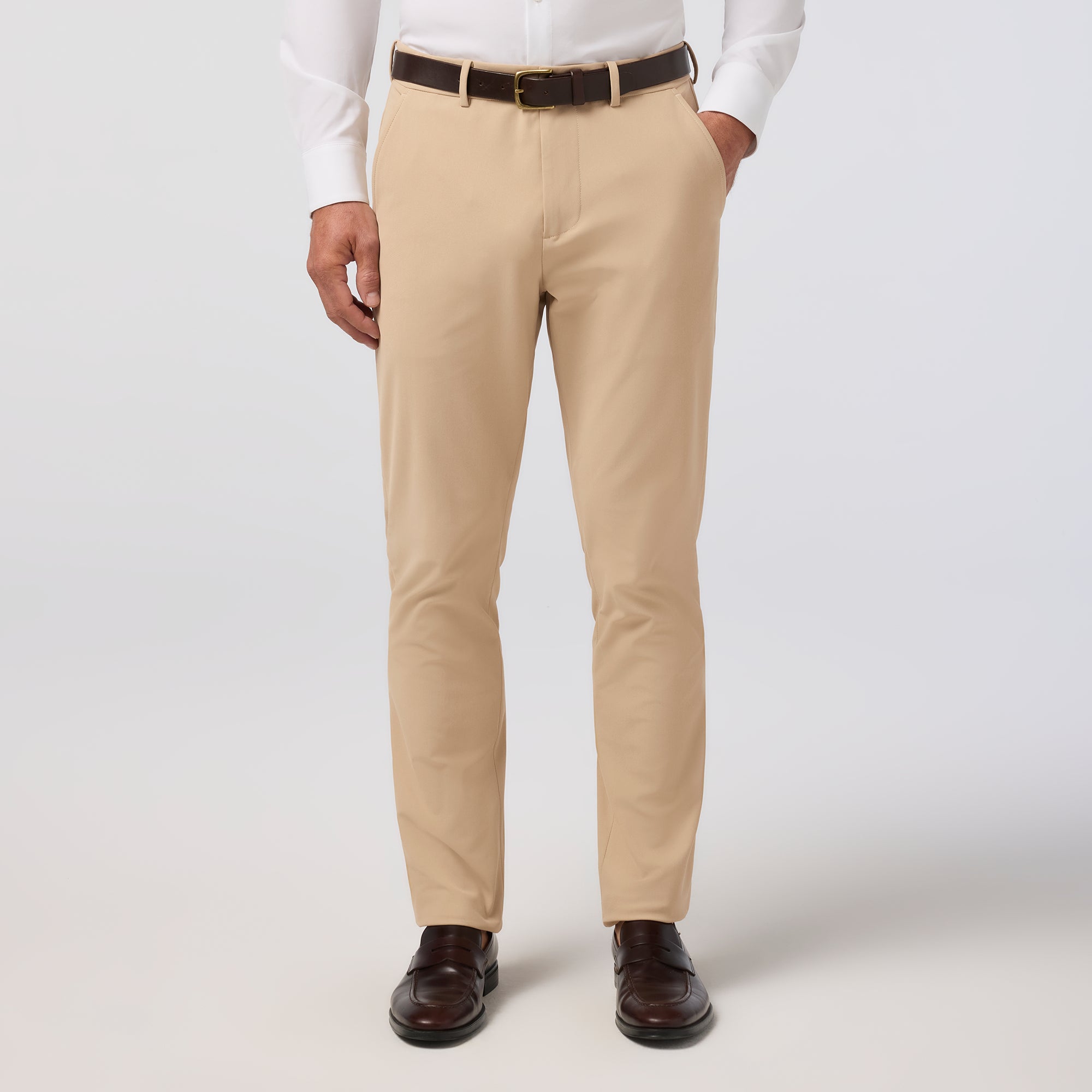 Beige dress pants worn with a white shirt and brown shoes on a plain background