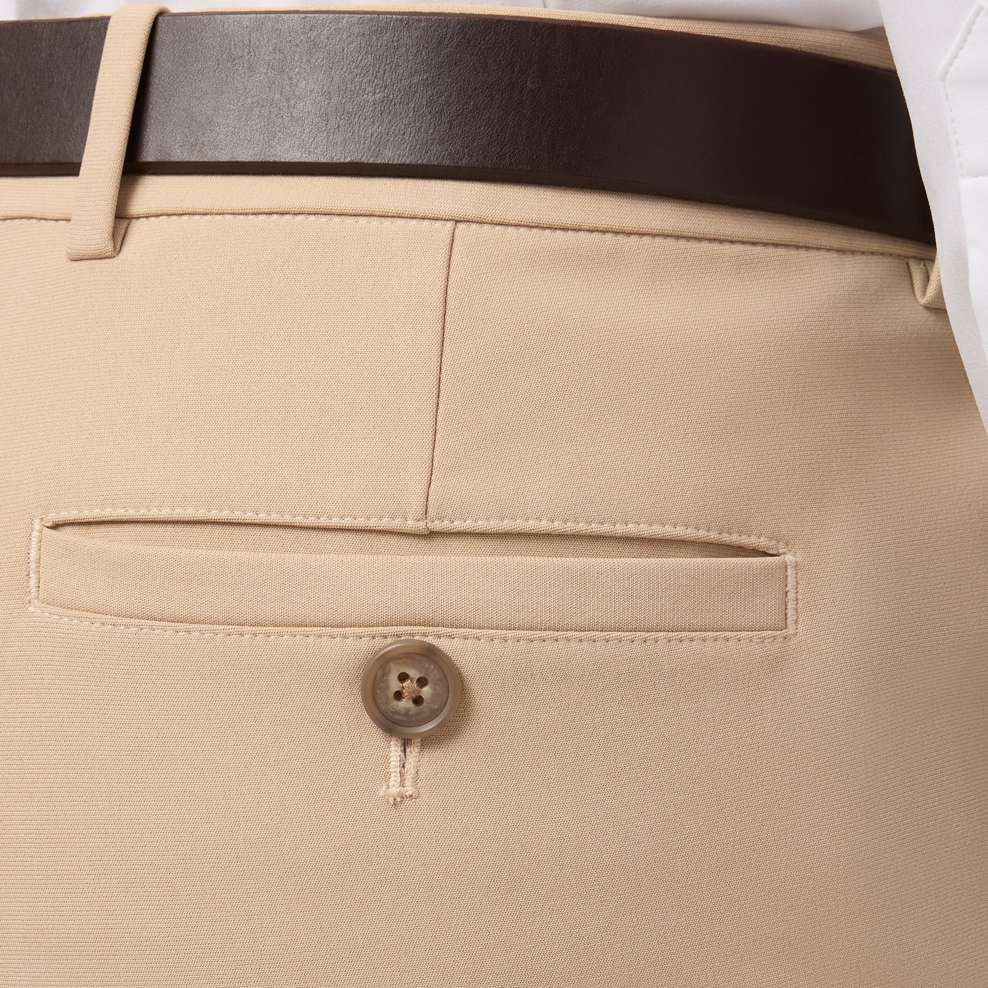 Close-up of beige pants with a button and belt on a light gray background