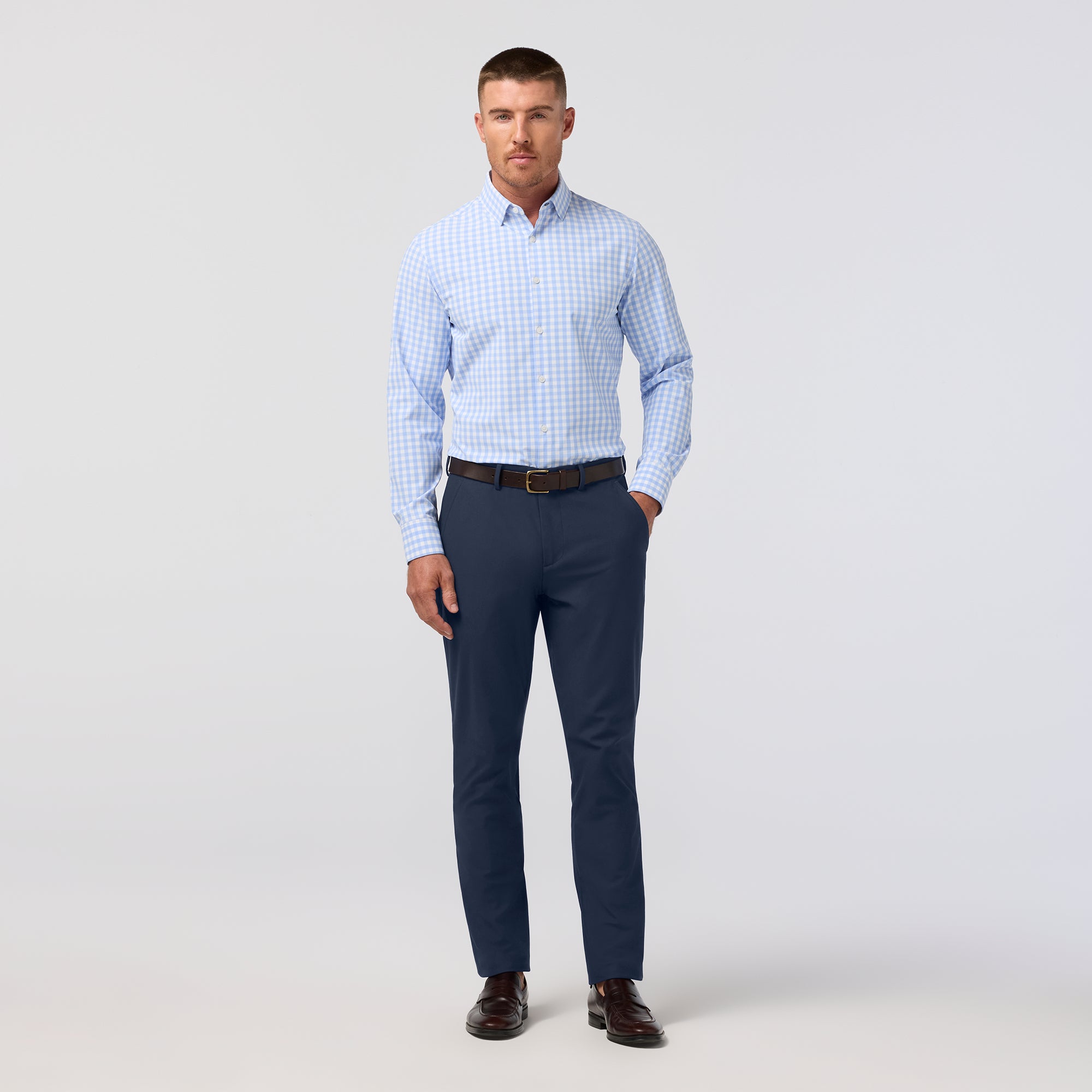 Man wearing a light blue checkered shirt and navy pants on a white background