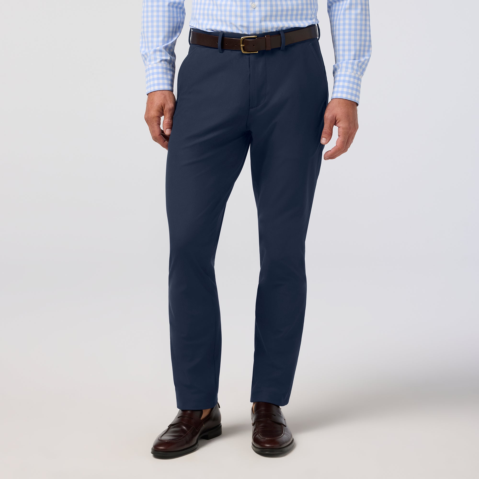 Navy dress pants worn with a light blue checkered shirt and brown shoes on a white background