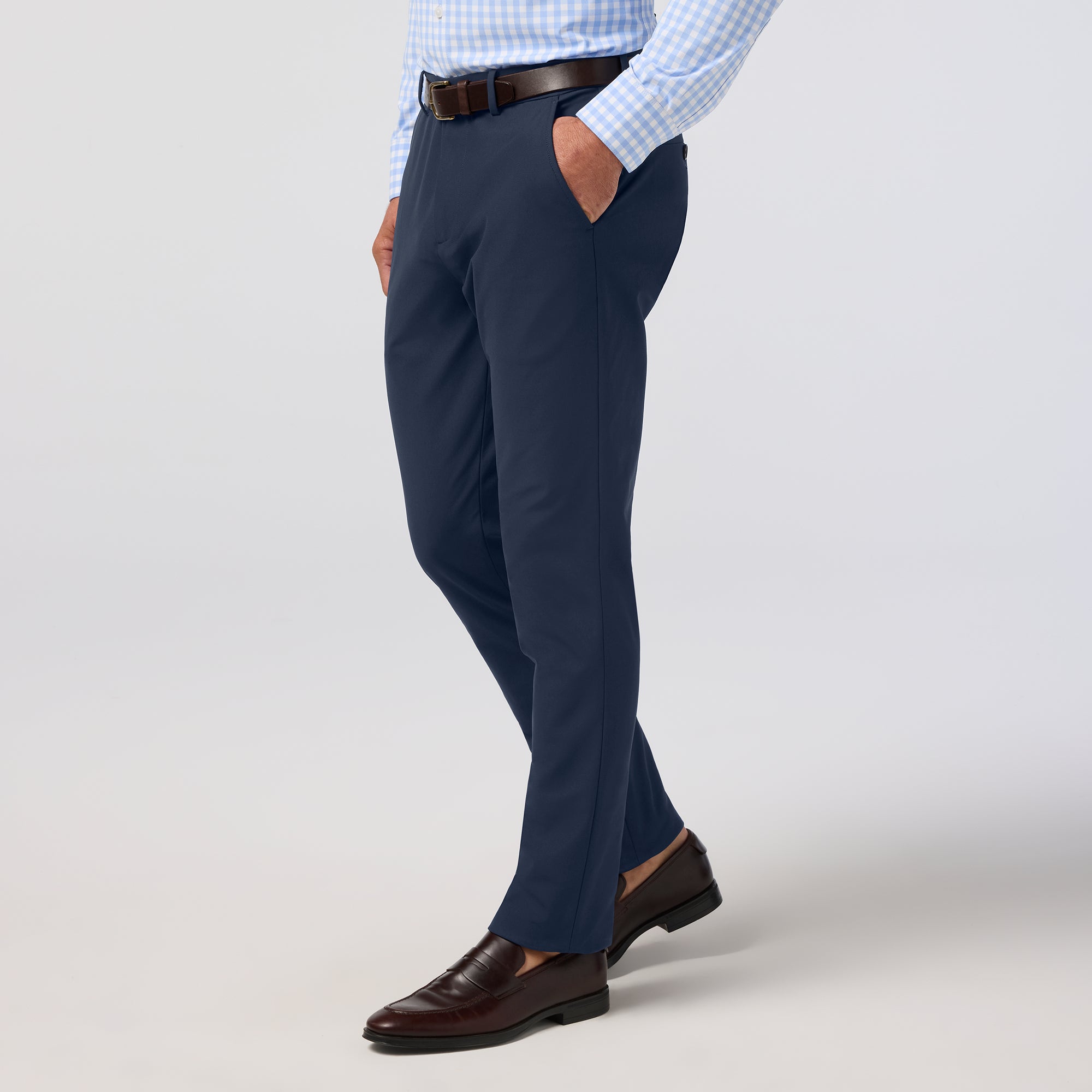 Person wearing navy dress pants with a checkered shirt and brown shoes on a light gray background
