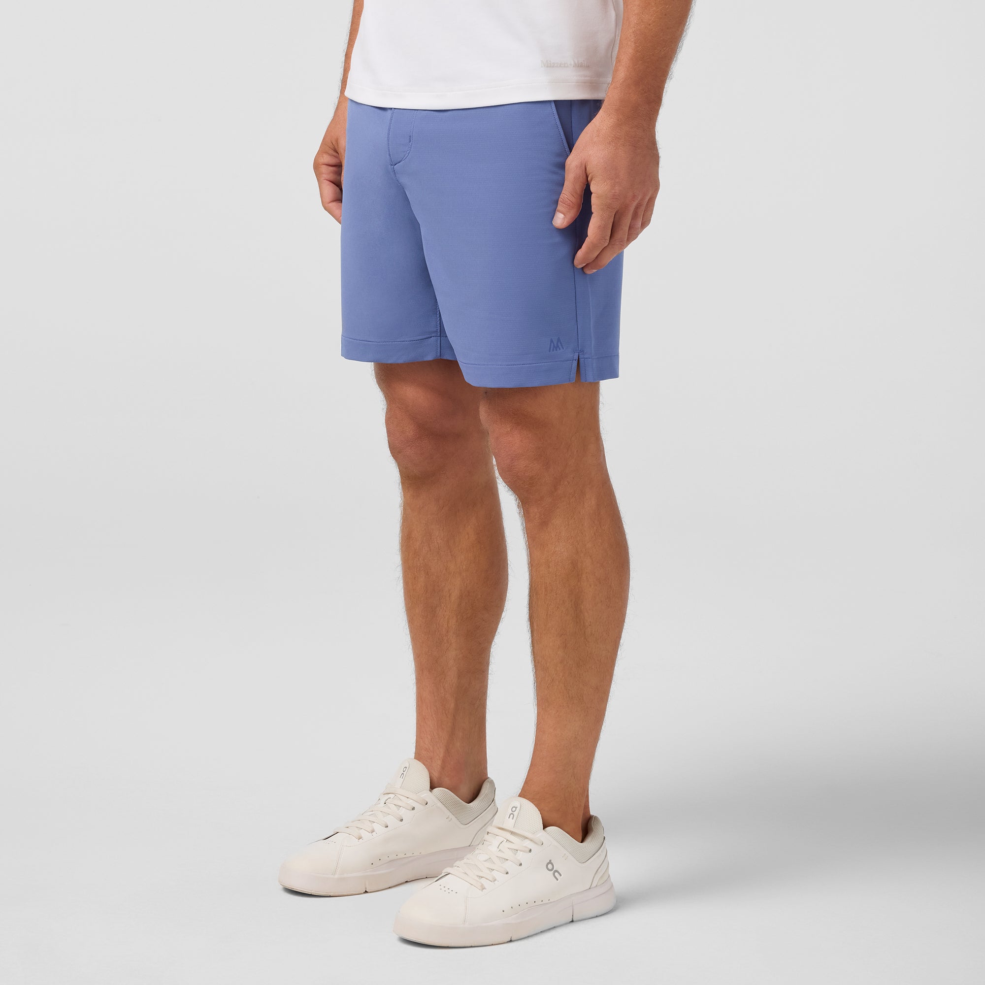Person wearing blue shorts and white sneakers on a plain background