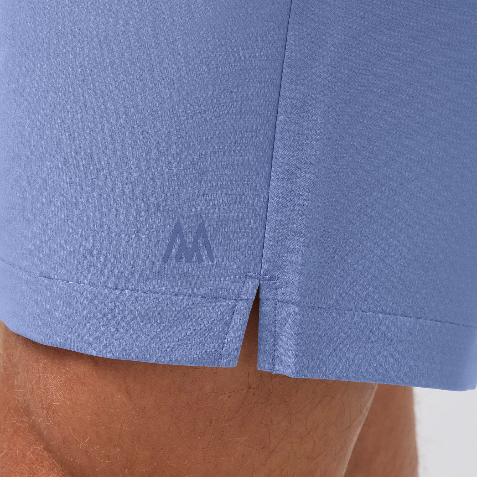 Close-up of a blue shorts with a logo on the hem against a neutral background