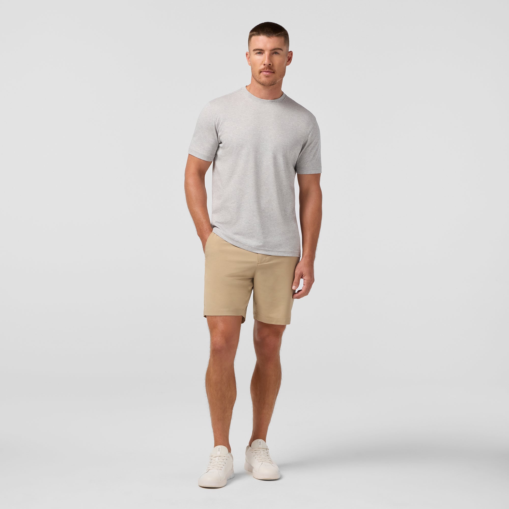 Man wearing a gray t-shirt and beige shorts on a plain background