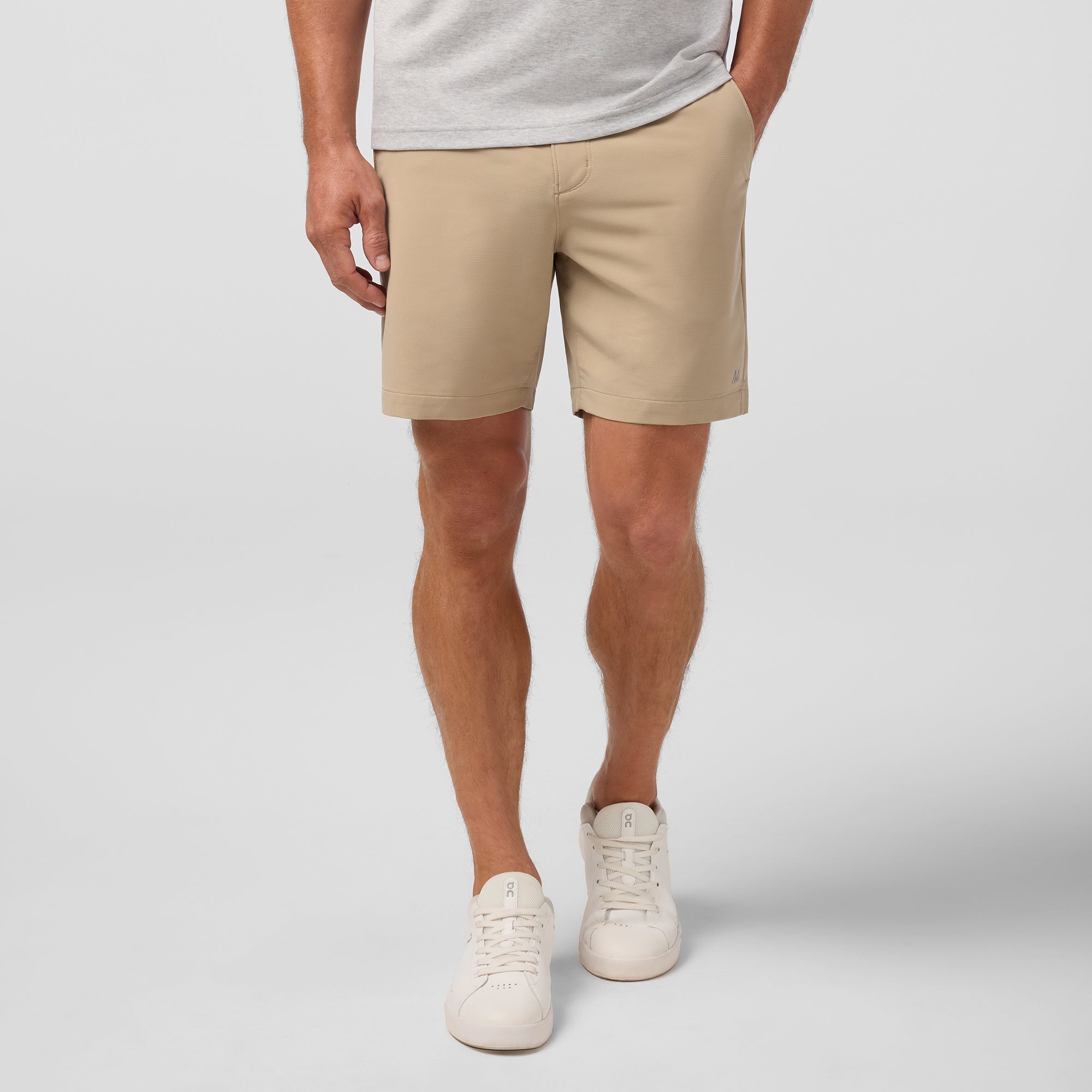 Person wearing beige shorts and white sneakers on a plain background