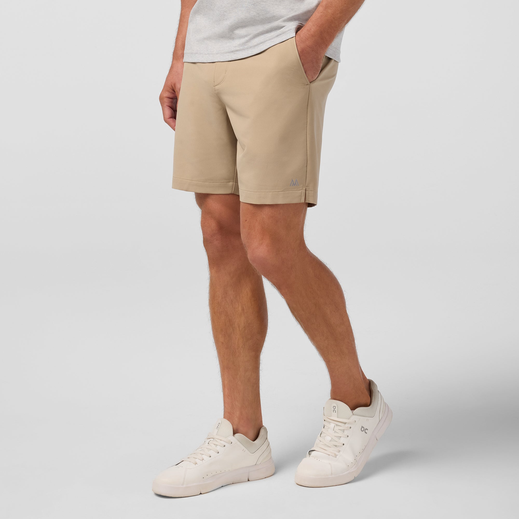Person wearing beige shorts and white sneakers on a plain background
