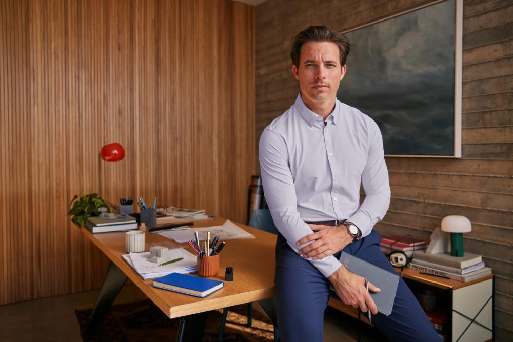 Man wearing a dress shirt sat on a desk holding a notebook