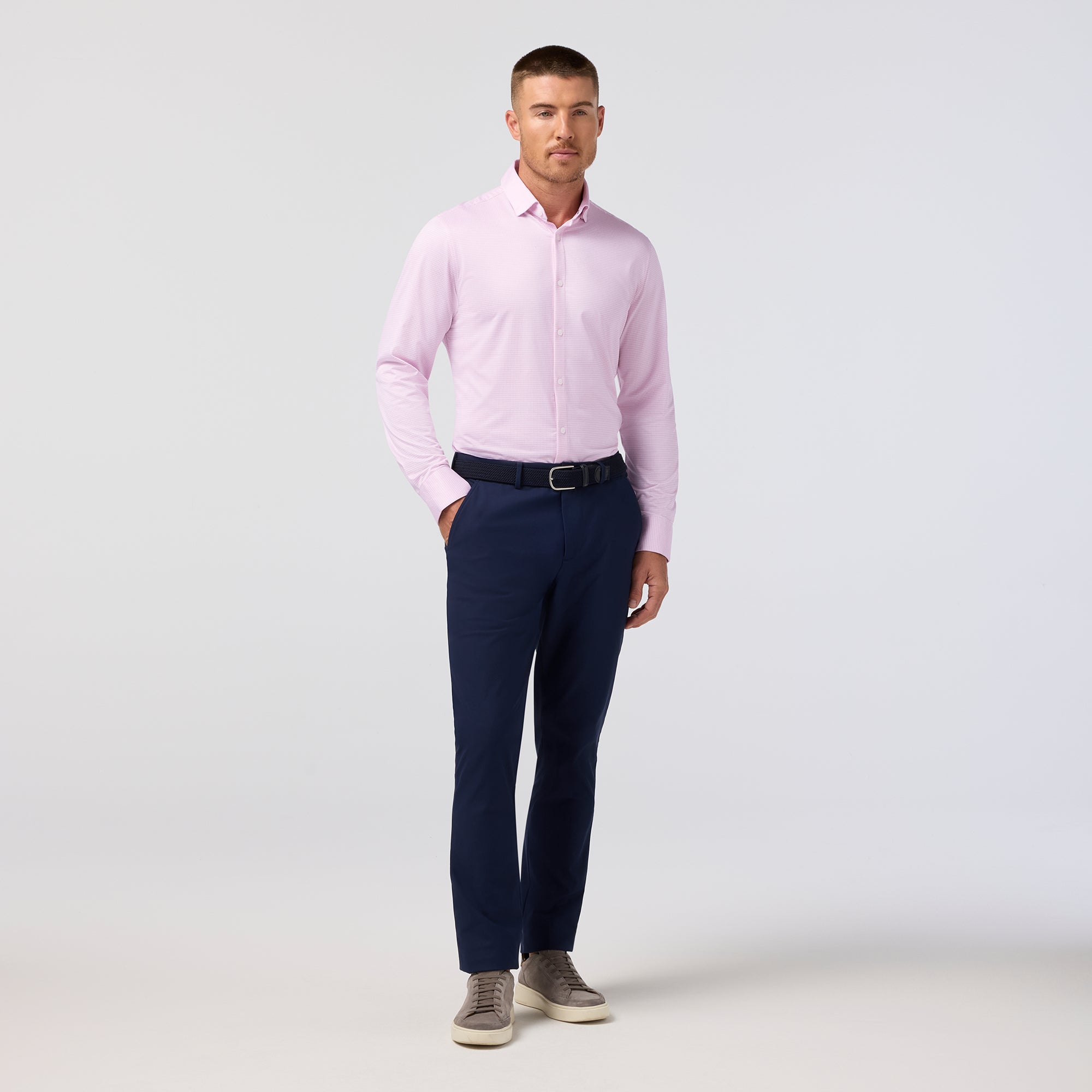 Man wearing a light pink dress shirt and navy pants on a white background