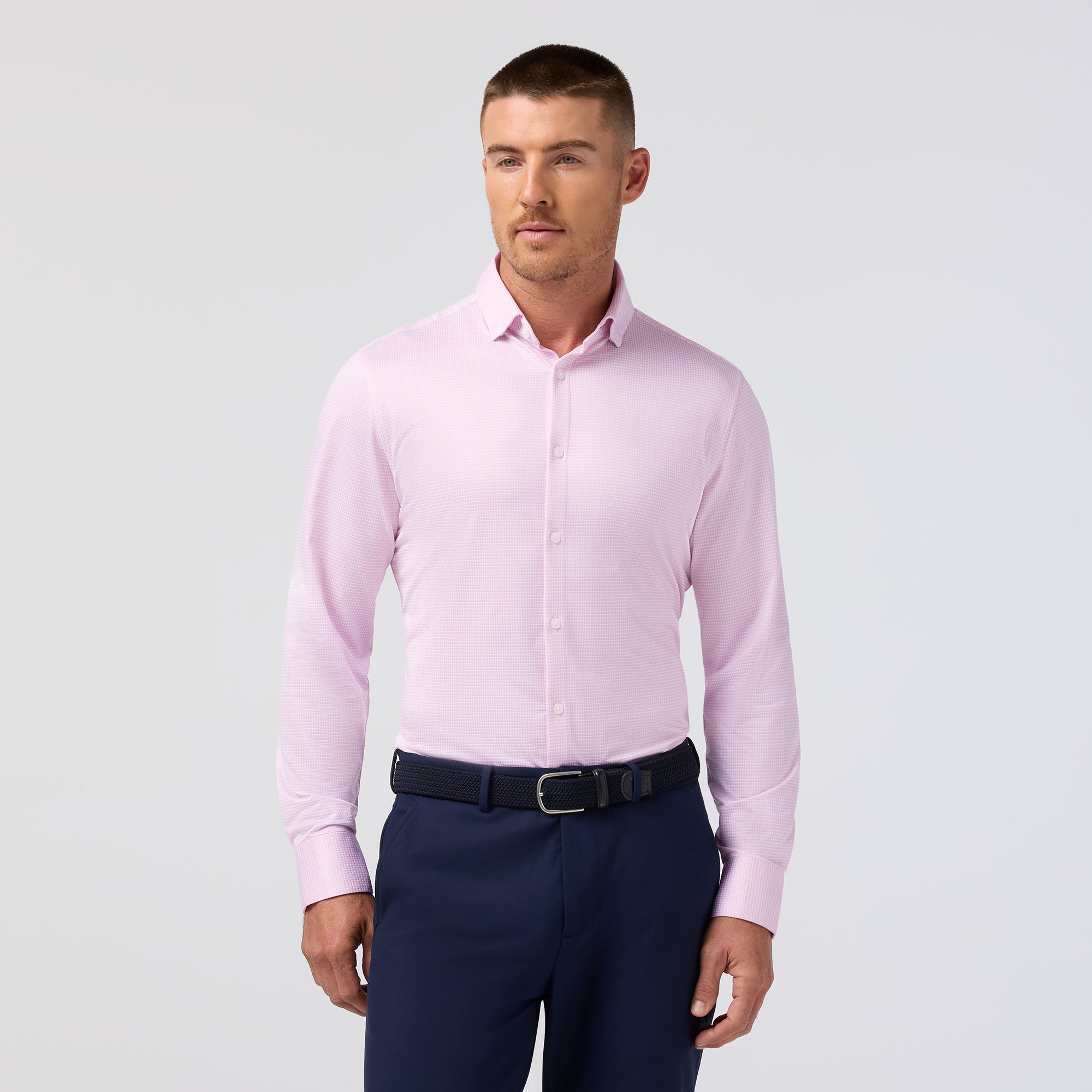 Man wearing a light pink dress shirt and navy pants on a gray background