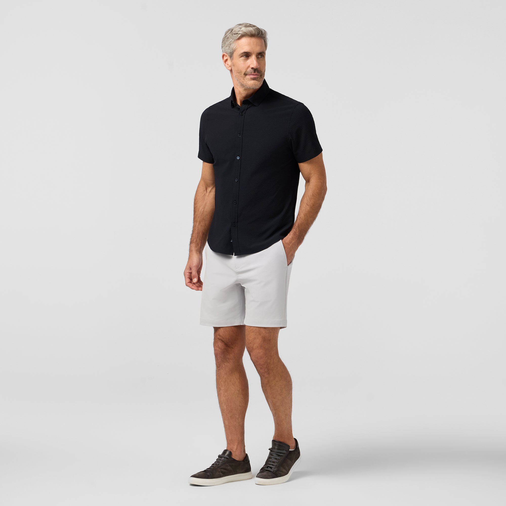 Man wearing a black shirt and light gray shorts on a white background