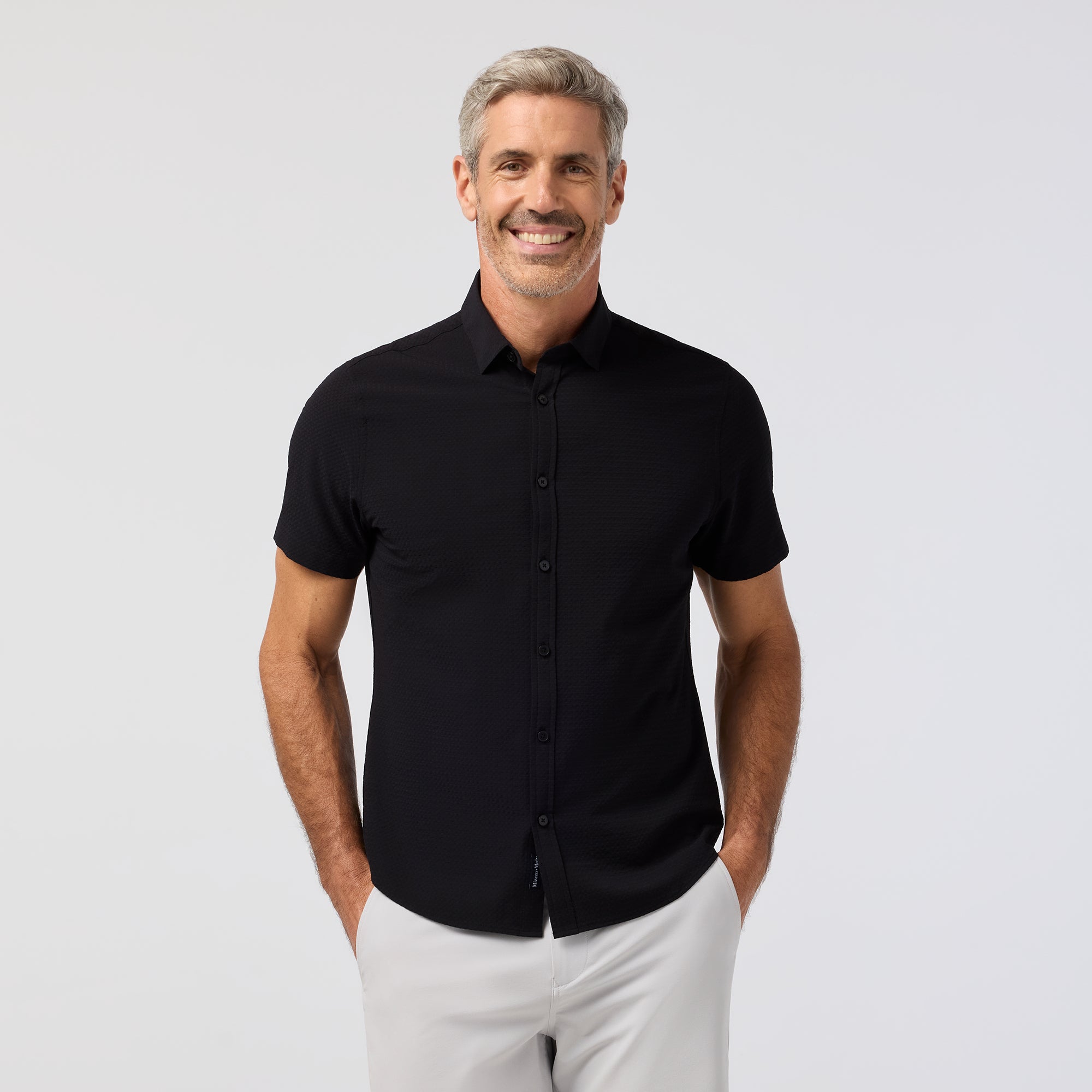 Man wearing a black short-sleeve shirt and white pants on a light gray background