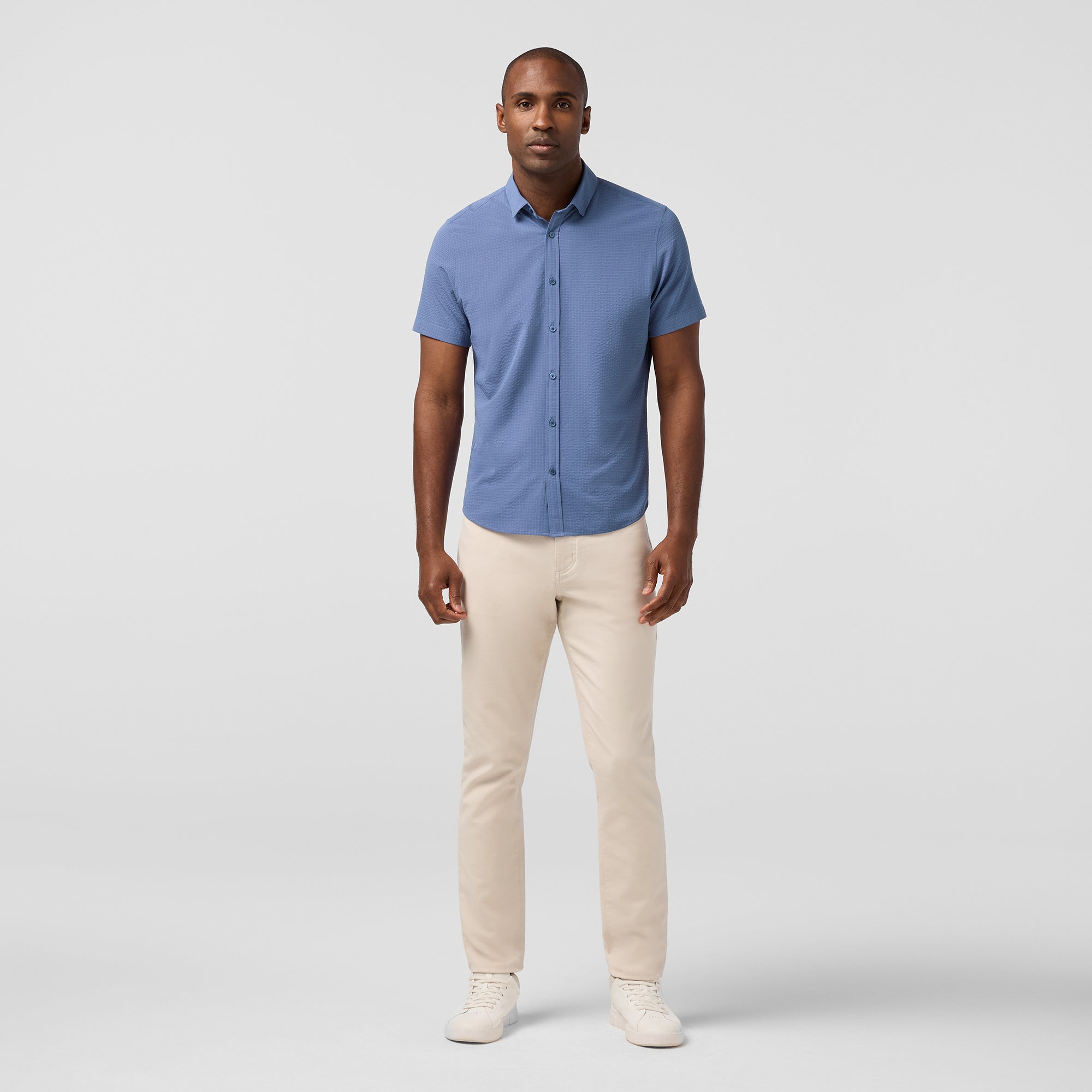 Man wearing a blue shirt and beige pants on a light gray background