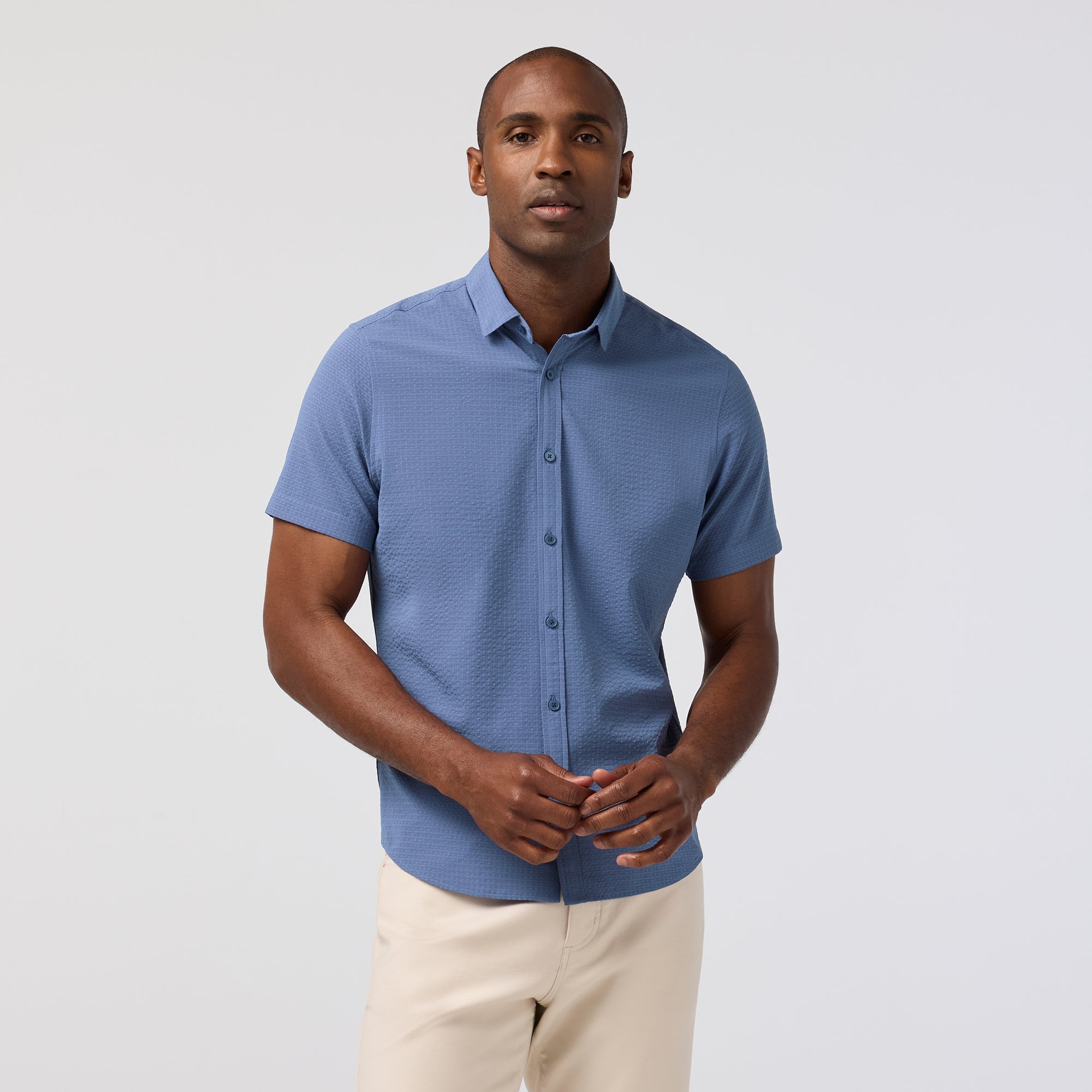 Man wearing a blue short-sleeve shirt and beige pants on a light gray background