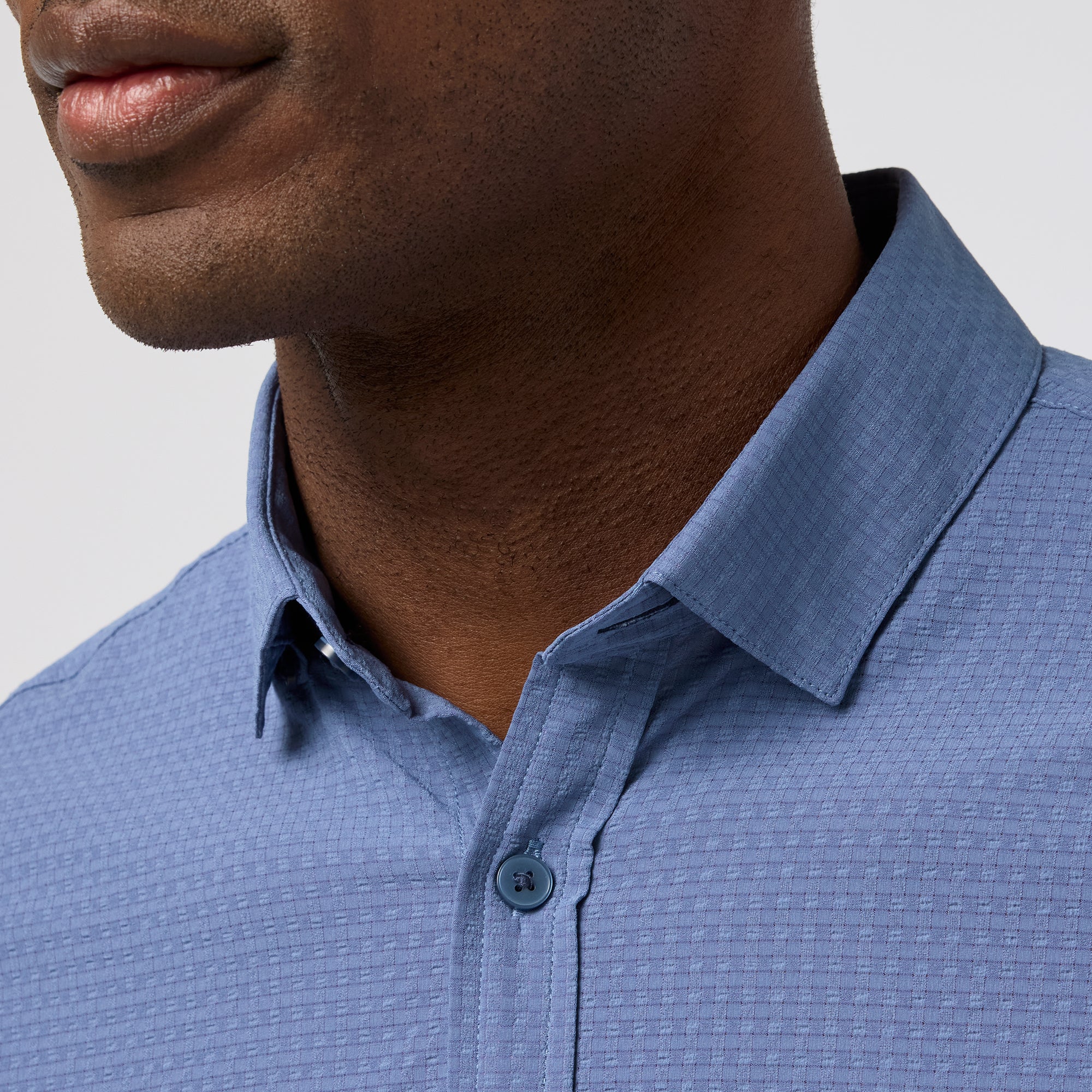 Close-up of a person wearing a blue textured shirt with a neutral background