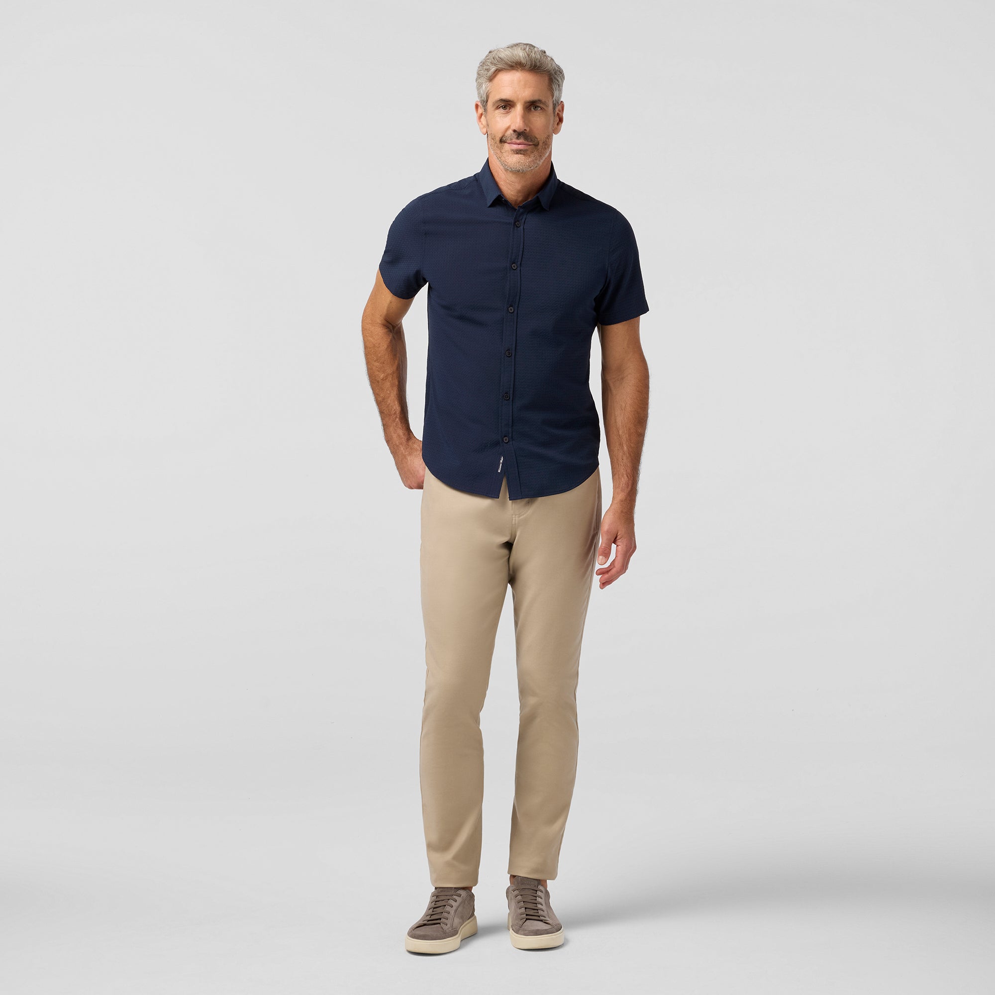 Man wearing a navy shirt and beige pants on a light gray background