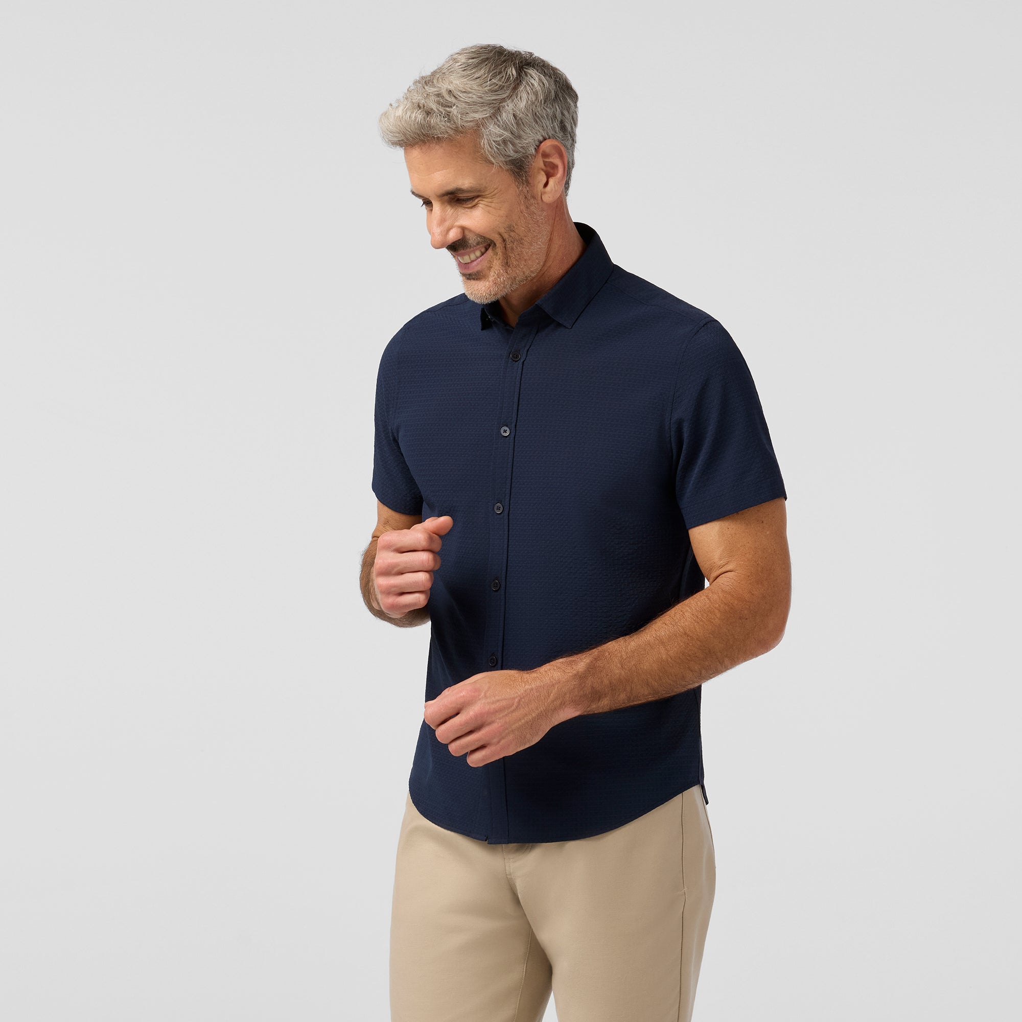 Man wearing a navy shirt and beige pants on a light gray background