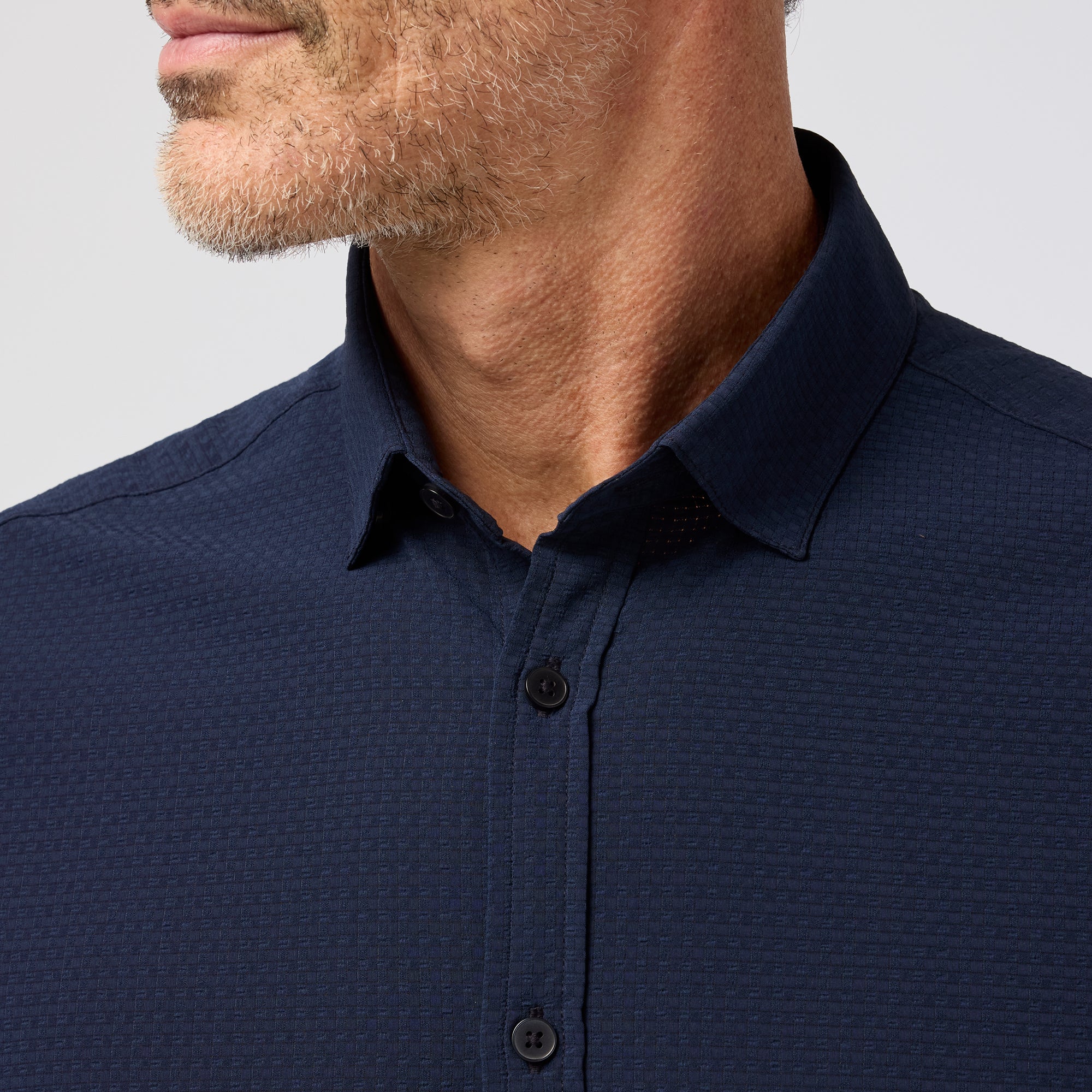 Man wearing a navy blue textured shirt against a light gray background