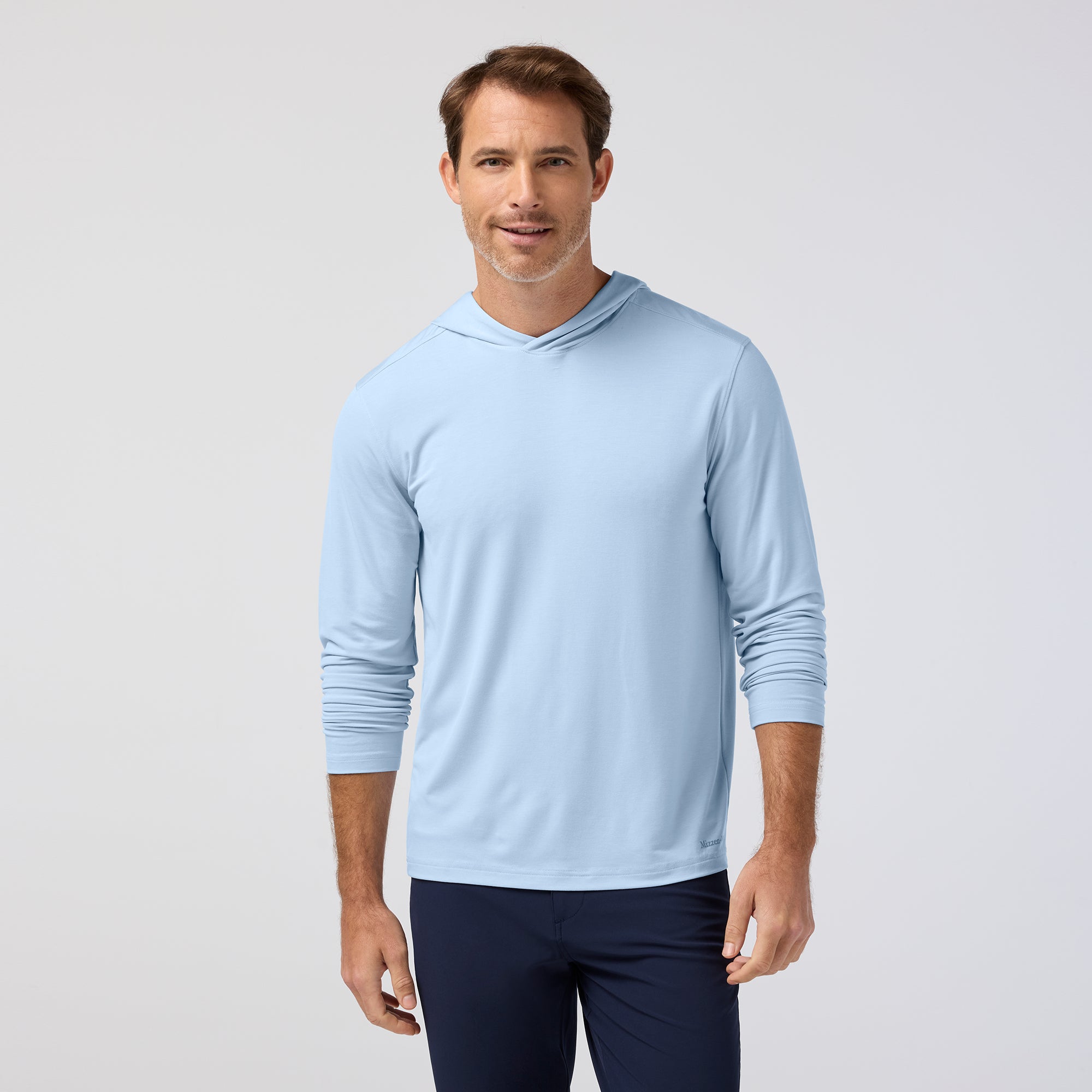 Man wearing a light blue hoodie and navy pants on a plain background